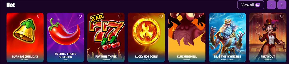 “Casino ‘Hot’ games carousel on a purple interface showing slot tiles: Burning Chilli 243, 40 Chilli Fruits Superior, Fortune Three, Lucky Hot Coins, Clucking Hell, Zeus the Invincible, and Freak Out, with a ‘View all (42)’ button and navigation arrows.”