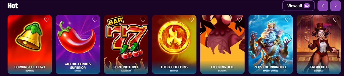 “Casino ‘Hot’ games carousel on a purple interface showing slot tiles: Burning Chilli 243, 40 Chilli Fruits Superior, Fortune Three, Lucky Hot Coins, Clucking Hell, Zeus the Invincible, and Freak Out, with a ‘View all (42)’ button and navigation arrows.”